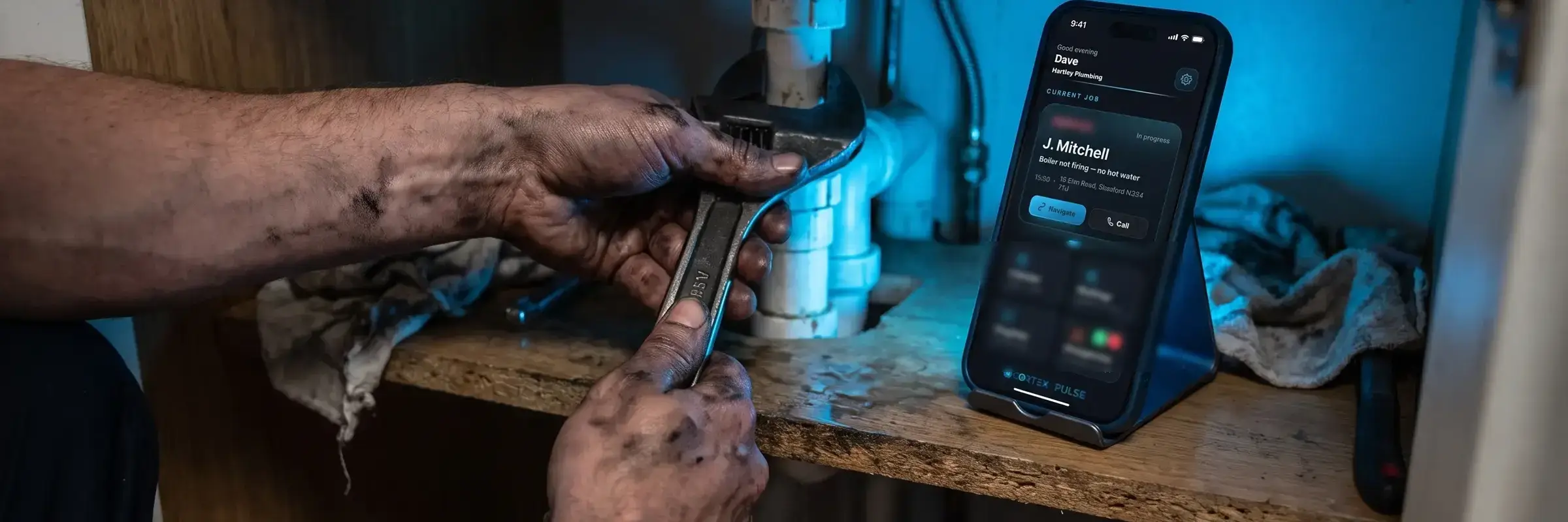 A plumber working under a sink with the job open on the phone beside him